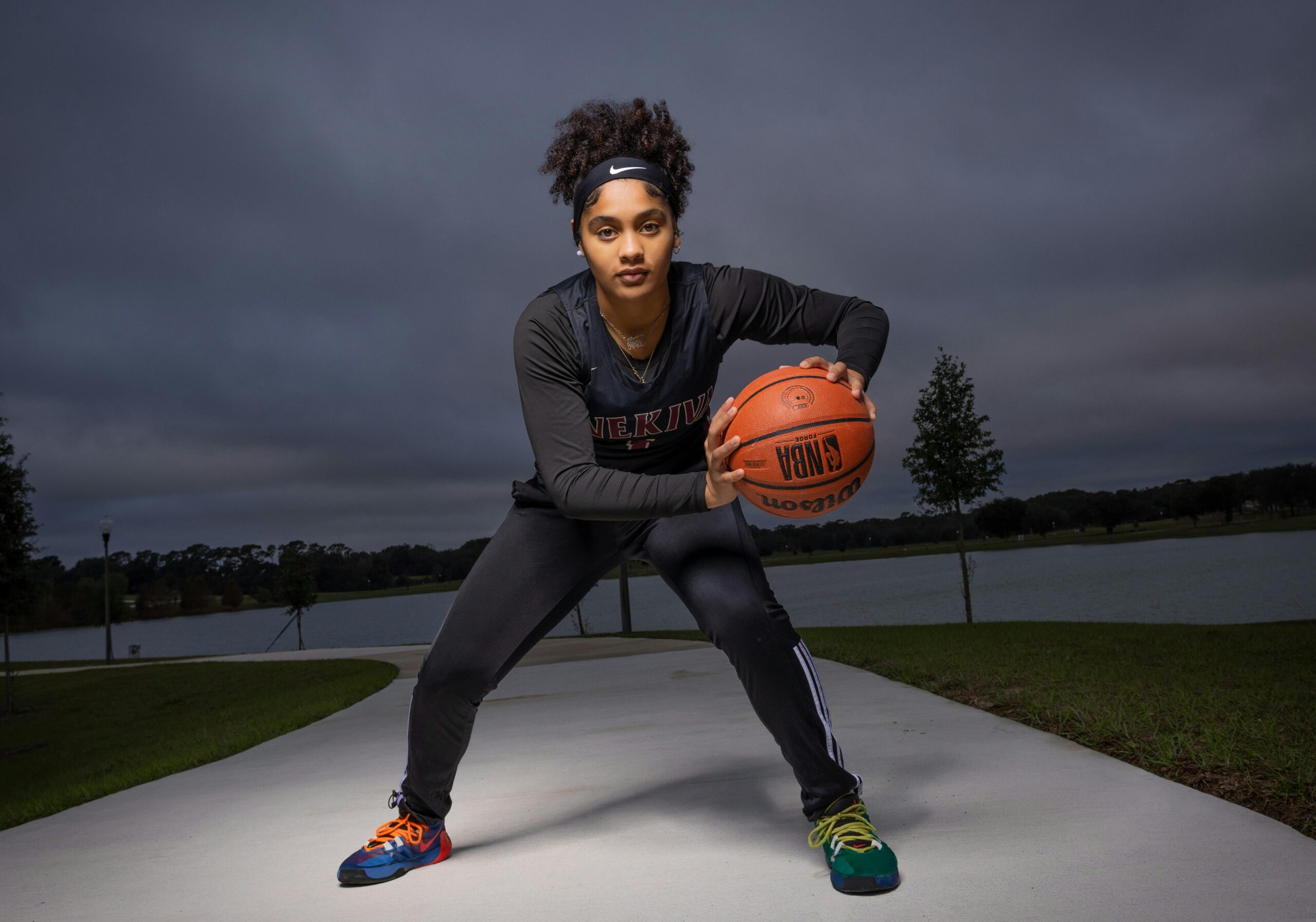 Mulher preta, com vestes pretas, posicionada com uma bola de basquete